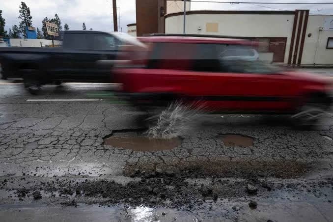 A car splashing through a water-filled pothole on a cracked road