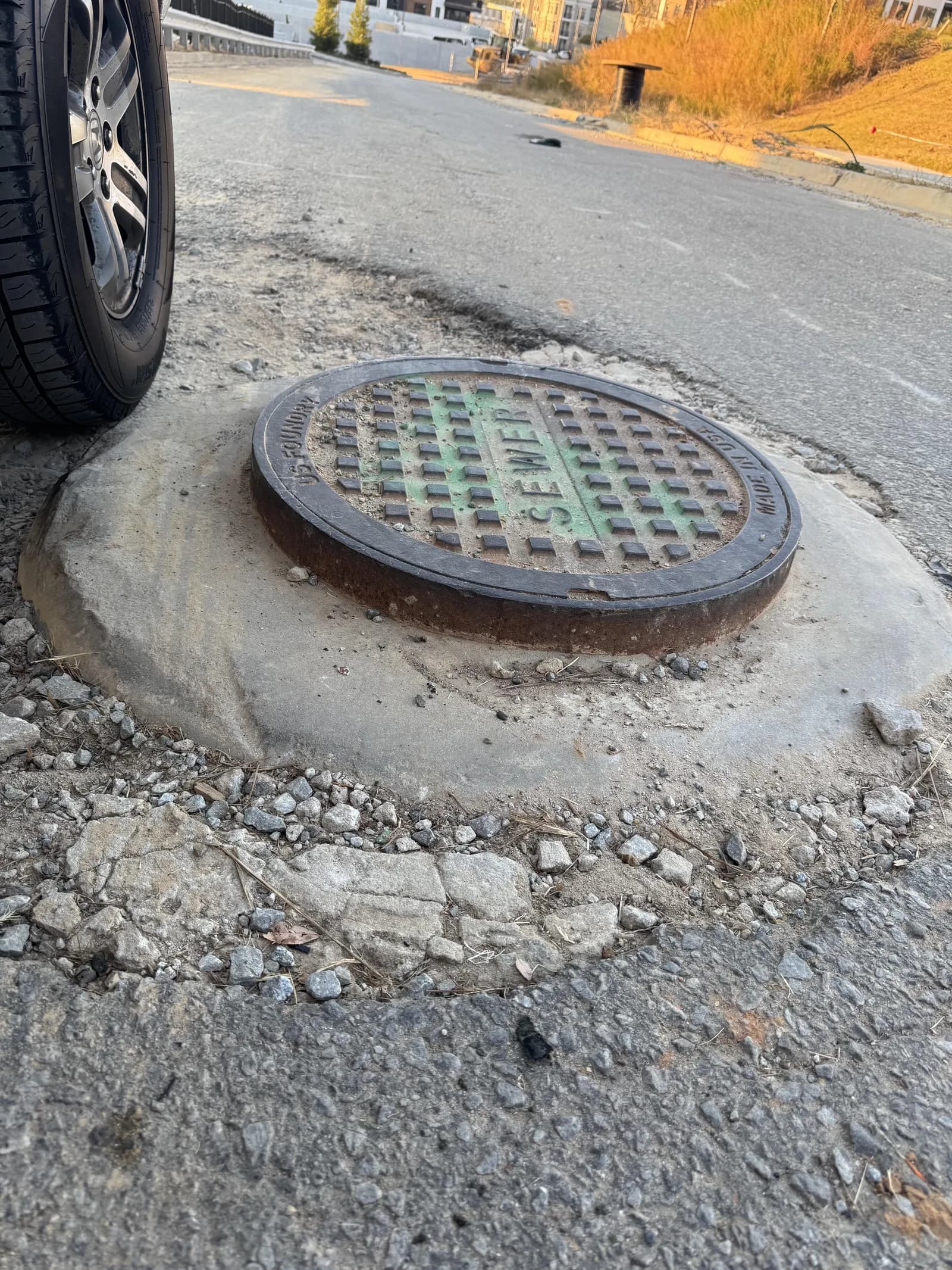 A sewer manhole cover left standing proud of the road, the asphalt broken away around it