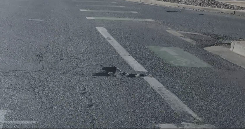 A frame of cracked asphalt with a pothole opening across a lane line