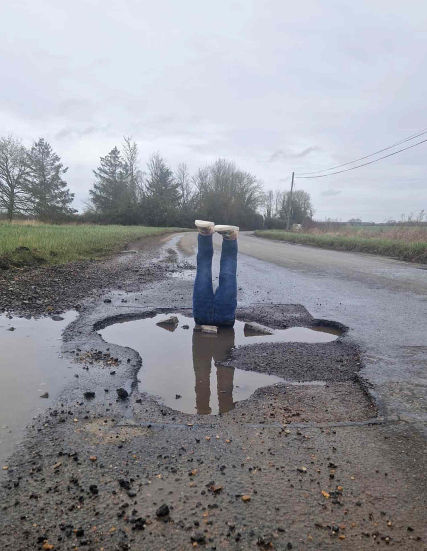 A resident staging a protest photo in a water-filled pothole